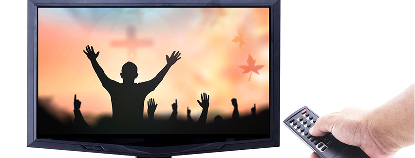 a hand holding a remote control pointing at a television showing people with their arms raised up in front of a cross