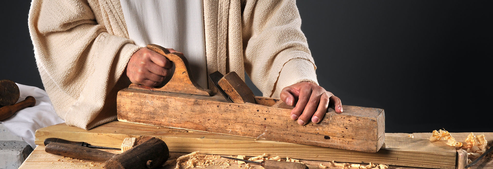 a carpenter dressed in an old robe like Jesus wood working with old hand tools