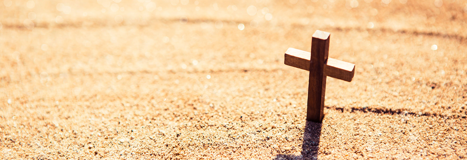 a small wooden cross stuck in the sand on a sunny beach