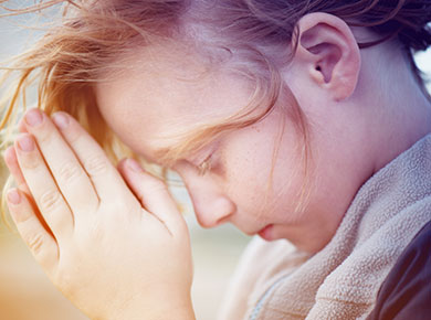 a red haired child head bowed in prayer with hands clasped at the forehead