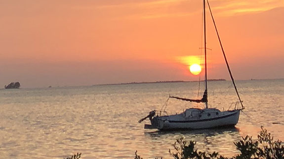 a sailboat anchored in the gulf with the sun setting behind it