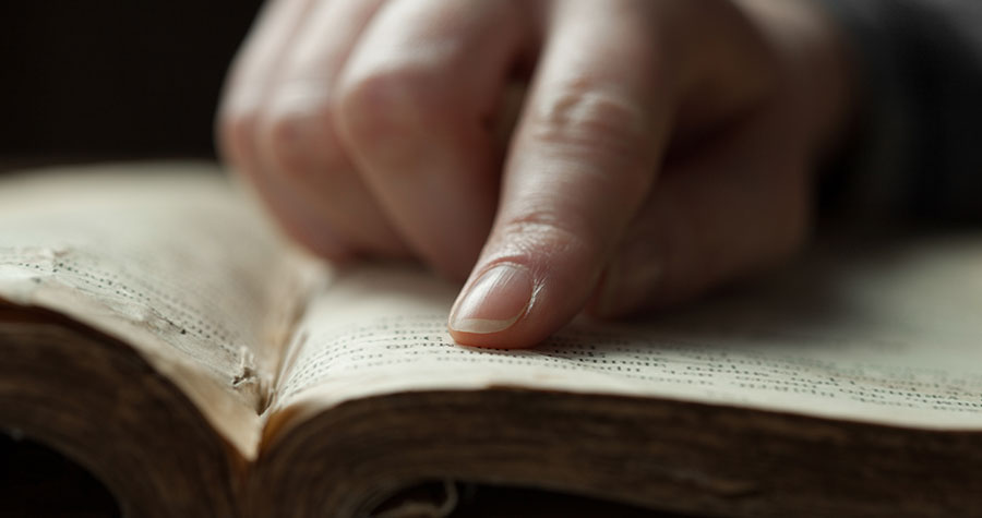 an index finger scanning words on a page of an old, well-read Bible
