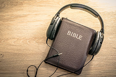 a brown leather Bible on a wooden desk with a pair of black headphones around the Bible