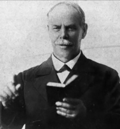 a black and white image of Smith Wigglesworth preaching pointing with his right index finger while reading from a Bible in his left hand